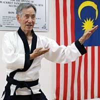 A man in a karate uniform is standing in front of a flag.