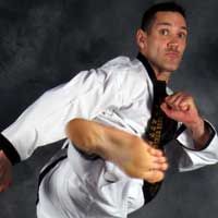 A man in a karate uniform is kicking his foot in the air.