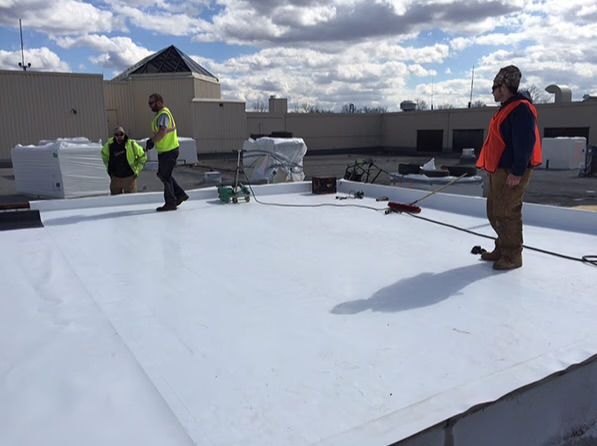 Worker installing dark roof shingles on a roof frame