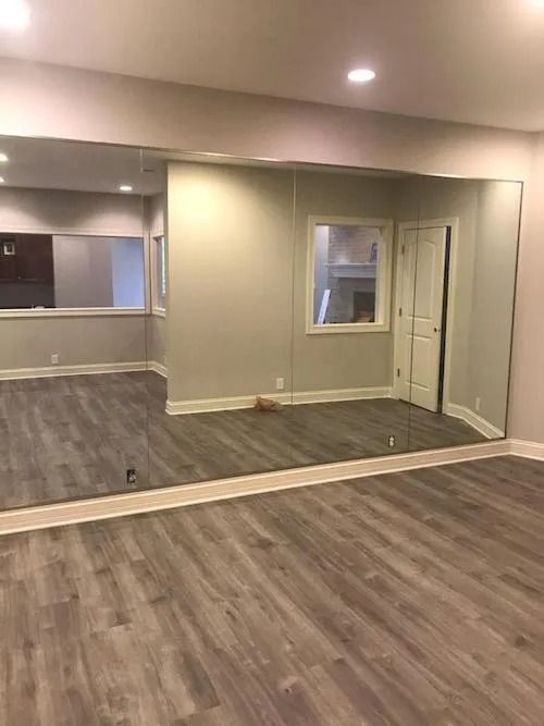 Room with gray wood flooring and wall mirrors; white walls and a doorway.