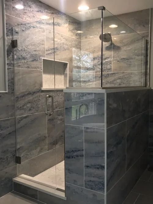 Glass-enclosed shower with blue-gray tiled walls and a built-in shelf.