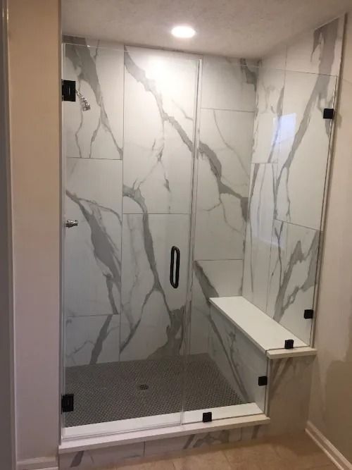 Glass-enclosed shower with white marble-look tiles. Includes a built-in bench and dark hardware.