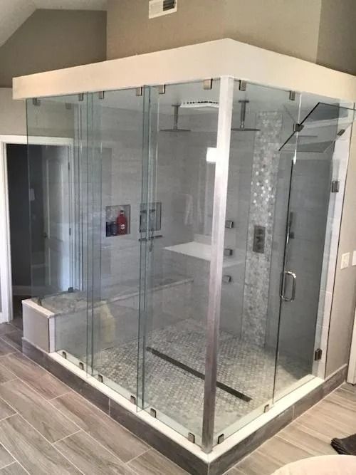 Corner shower with glass walls, bench, multiple showerheads, and pebble floor.