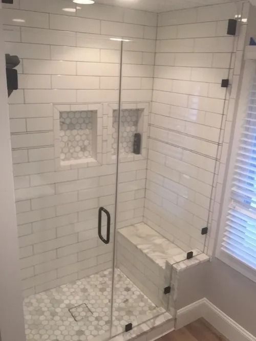 Modern white tiled shower with glass door and built-in marble bench.