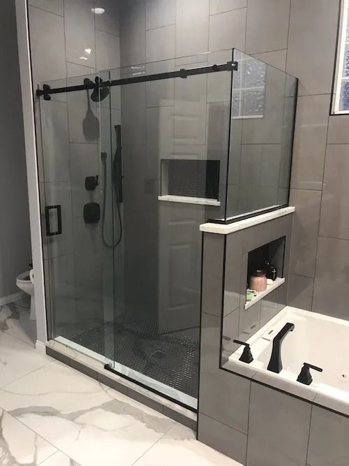 Modern gray tiled bathroom with glass shower, black fixtures, and built-in shelf.