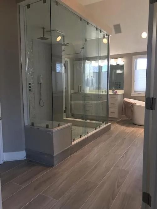 Large modern bathroom with glass shower enclosure, wood-look tile, and neutral walls.