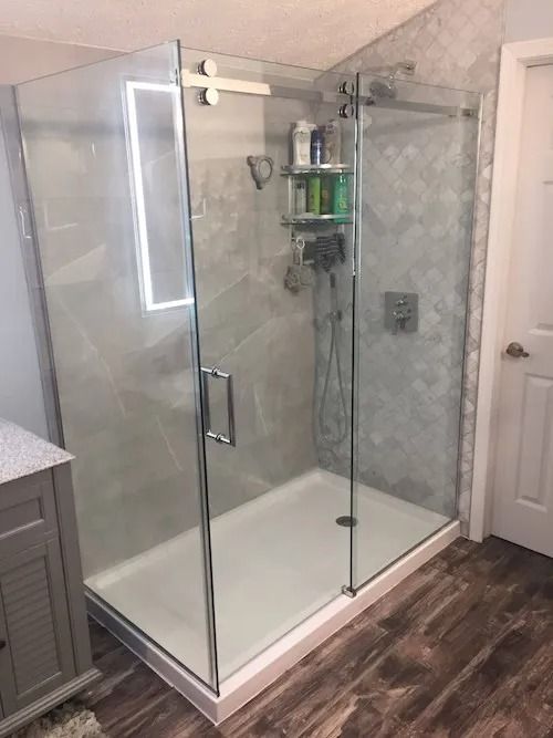 Glass shower enclosure with gray tiled walls, white base, and chrome fixtures in a bathroom.