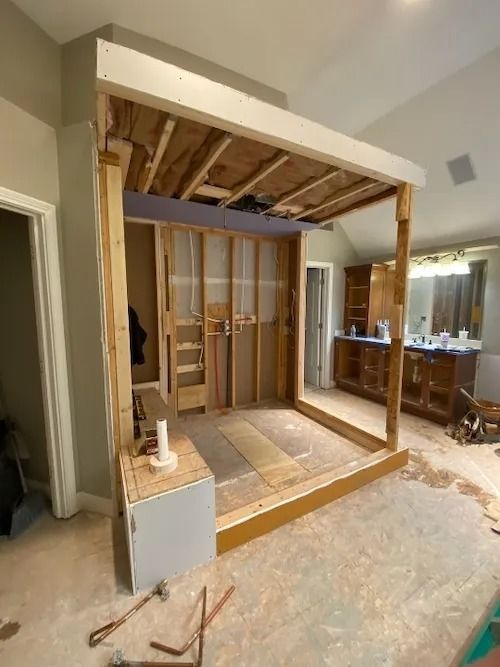 Framed structure under construction in a room, revealing studs, insulation, and partially finished surfaces.
