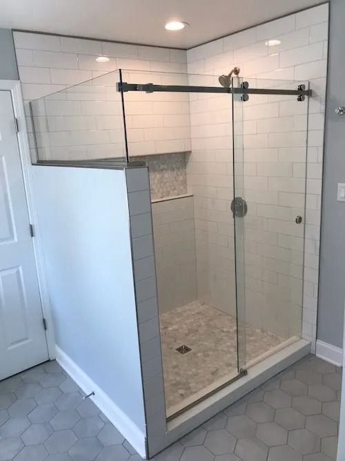 Modern shower with glass door and black hardware, white subway tile, and grey hexagonal floor tiles.