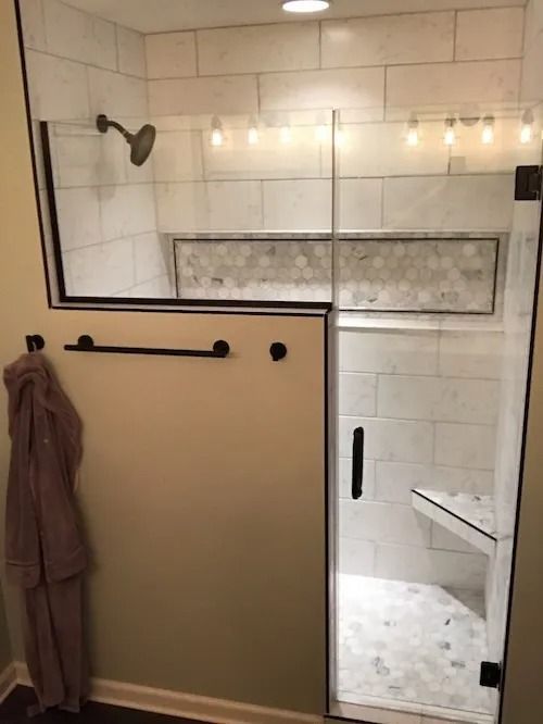 Modern bathroom with white tiled shower, glass door, bench, and towel rack.