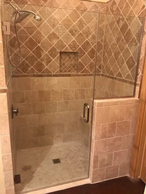 Shower with clear glass door and tan tile walls.