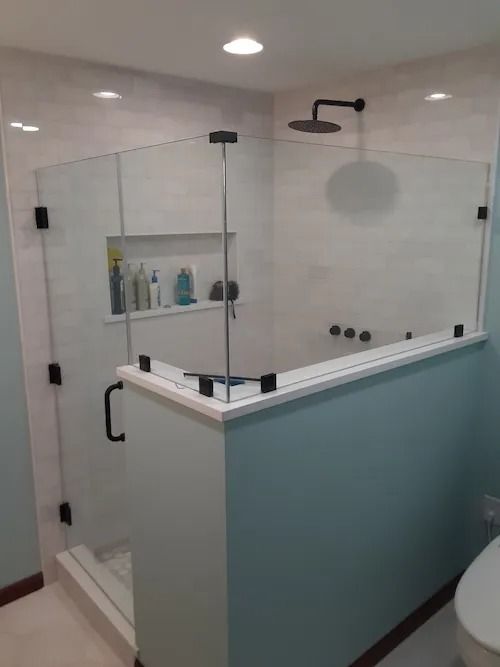 Modern glass shower with black fixtures and built-in shelf in a light blue bathroom.