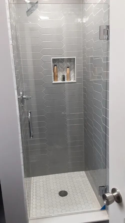Glass-enclosed shower with gray tiled walls and a built-in shelf holding toiletries.