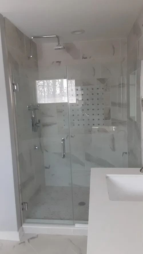 Modern glass shower with marble-look tile. Chrome fixtures, frosted accent, and a white countertop visible.