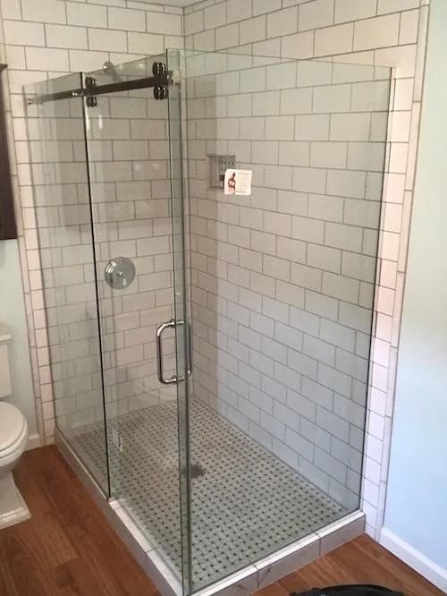 Glass shower enclosure with sliding door and subway tile walls.