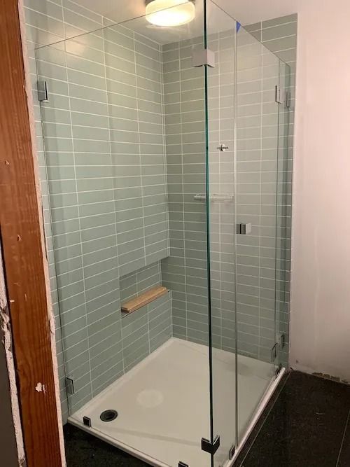 Glass shower enclosure with light green tiled walls and white shower base.