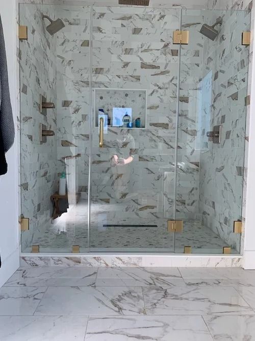 Marble shower with gold hardware and glass doors.