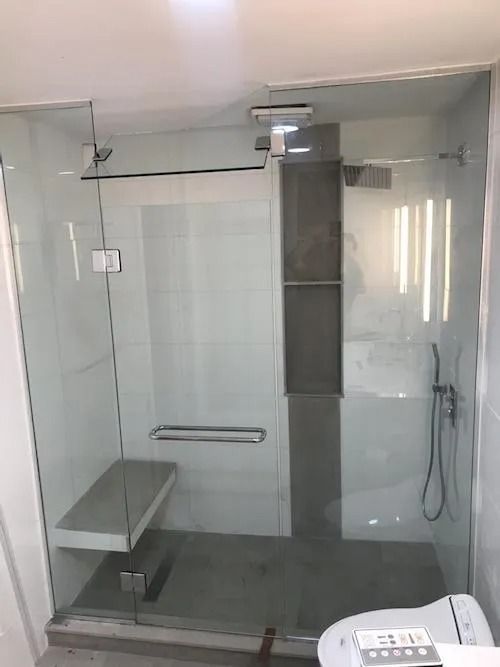 Glass shower enclosure with bench, shelf, and showerhead. Gray and white tiles.