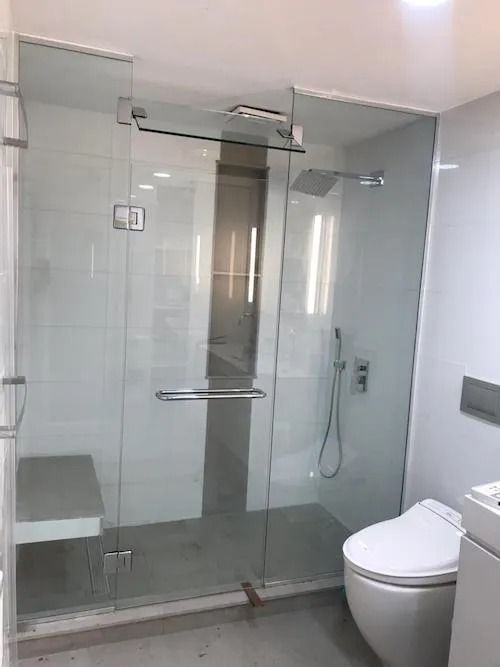 Glass shower enclosure in a modern bathroom with a toilet and a bench.