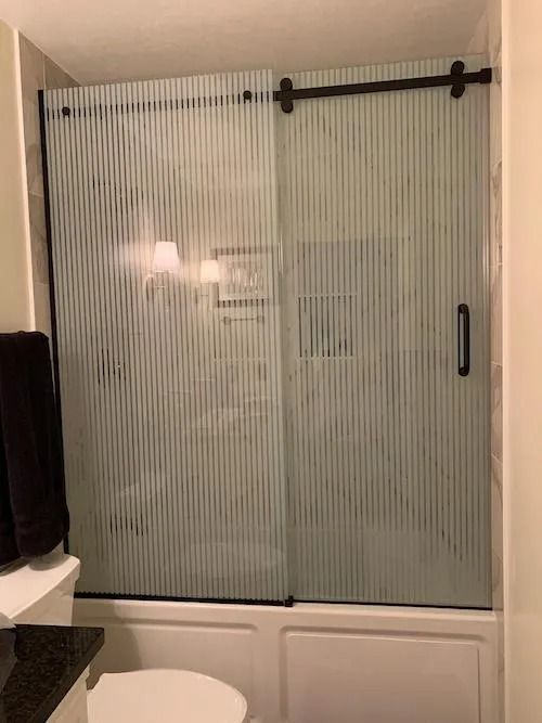 Sliding glass shower door with vertical striped pattern, black hardware.