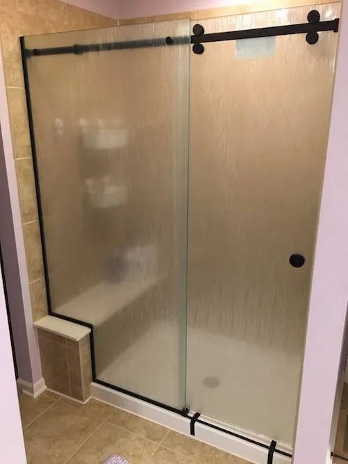 Frosted glass shower with black sliding door hardware, tan tile, and a built-in bench.
