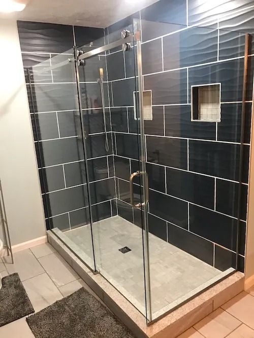 Modern shower with dark blue tiles, glass door, and gray floor.