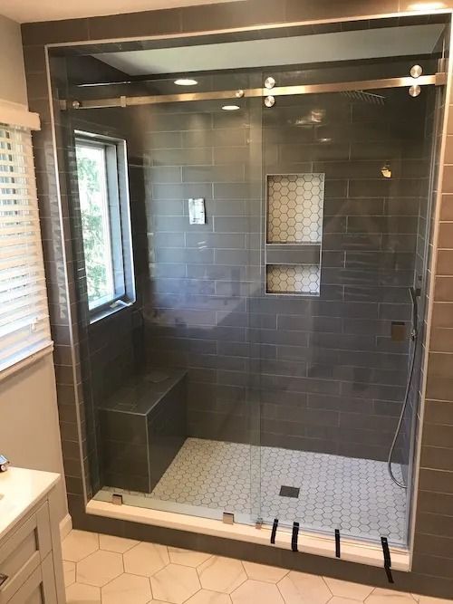 Modern shower with gray tiled walls, glass sliding door, built-in bench, and honeycomb tile floor.
