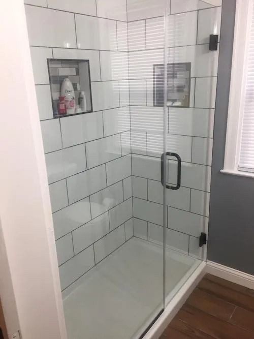 White tiled shower with glass door, black hardware, and two built-in shelves.