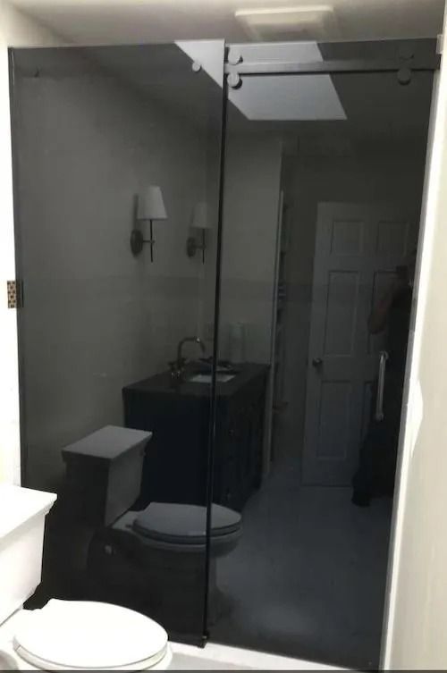 Black tinted glass shower doors in a bathroom, reflecting the toilet, sink, and door.