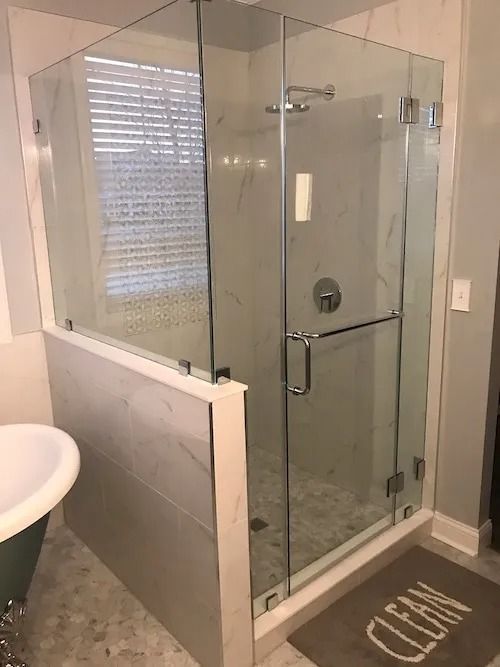 Glass shower enclosure with marble tile, chrome hardware, and a 