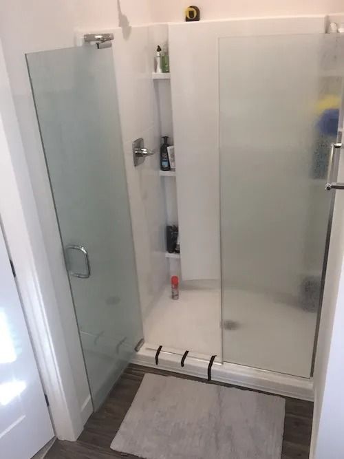 Glass shower enclosure with frosted glass doors, a built-in shelf, and a light-colored floor mat.