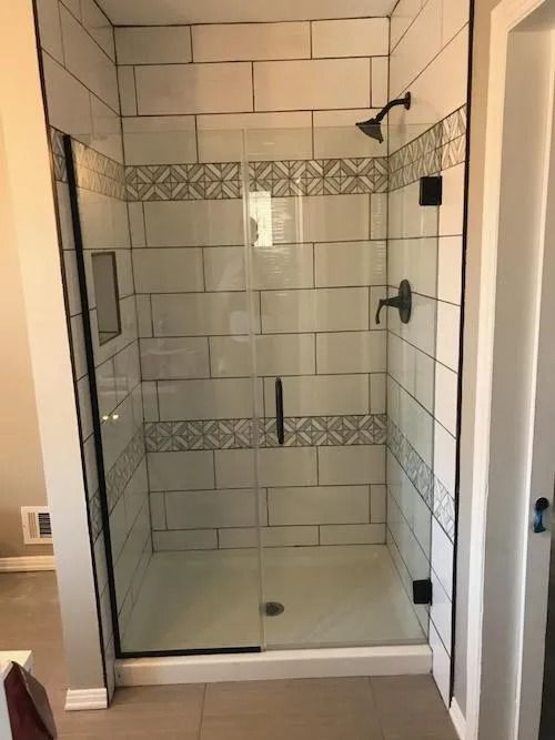 Glass shower with white tile, decorative border, and black fixtures.