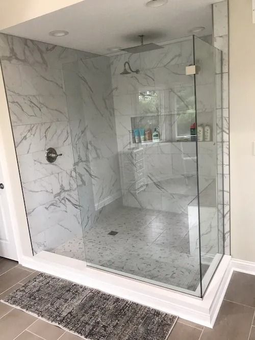 Modern marble-tiled shower with glass doors, built-in shelving, and a rain shower head. White and gray tones.