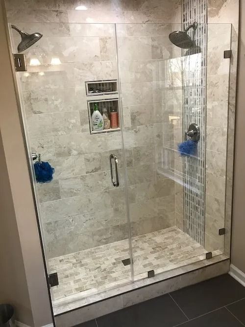 Modern walk-in shower with glass doors, two shower heads, neutral tile, built-in shelving, and dark floor.