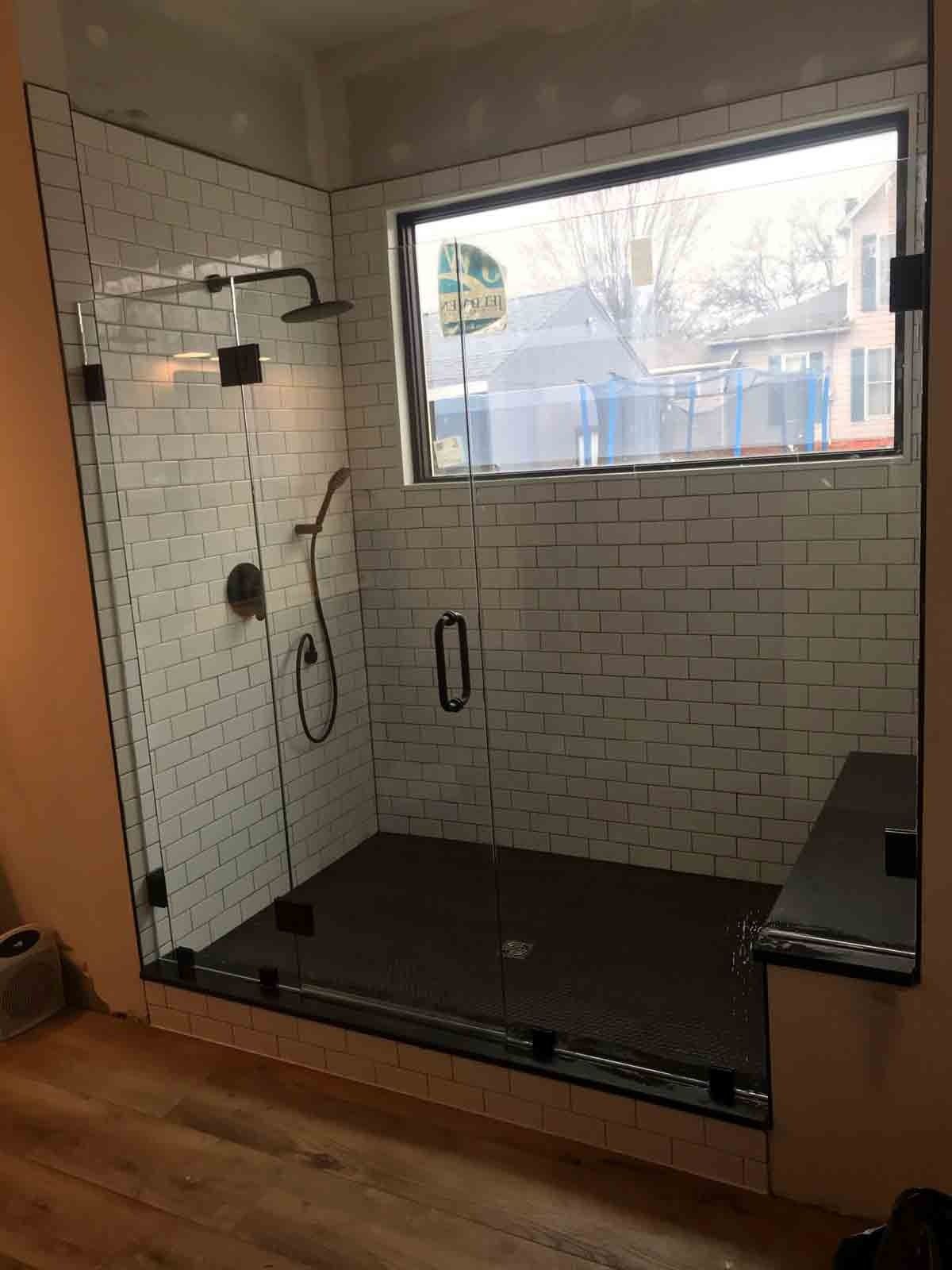 Modern shower with glass doors, white subway tile walls, dark floor, and window.
