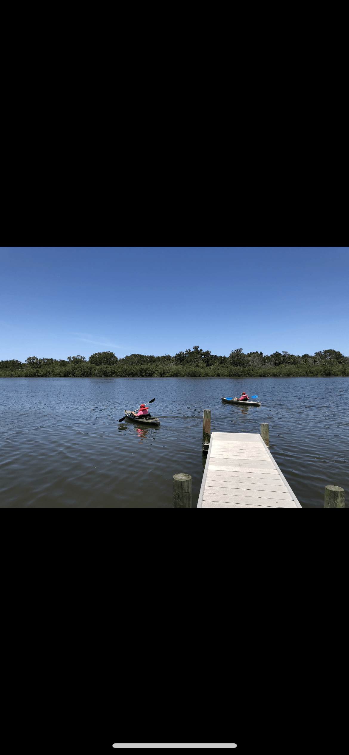 Two people are kayaking on a lake next to a dock.