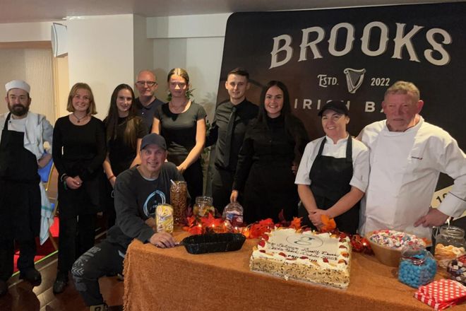 A group of people standing around a table with a cake on it.