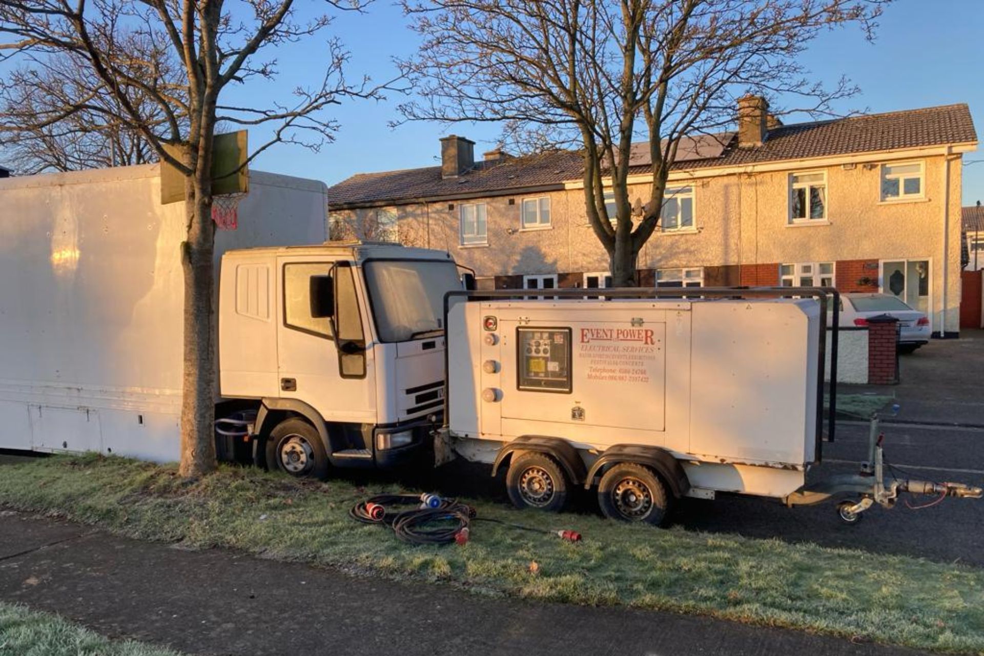 A white truck with a trailer attached to it is parked in front of a house.