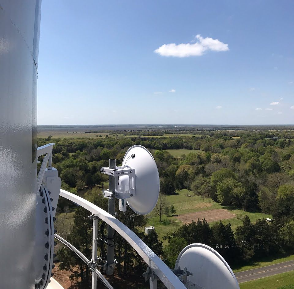 View from a communications tower. Dish antennas overlook a green rural landscape under a blue sky.