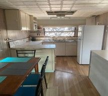 Kitchen With Wooden Floors, White Cabinets, a Refrigerator, and a Table With Chairs — Karumba Point Holiday Tourist Park in Karumba, QLD