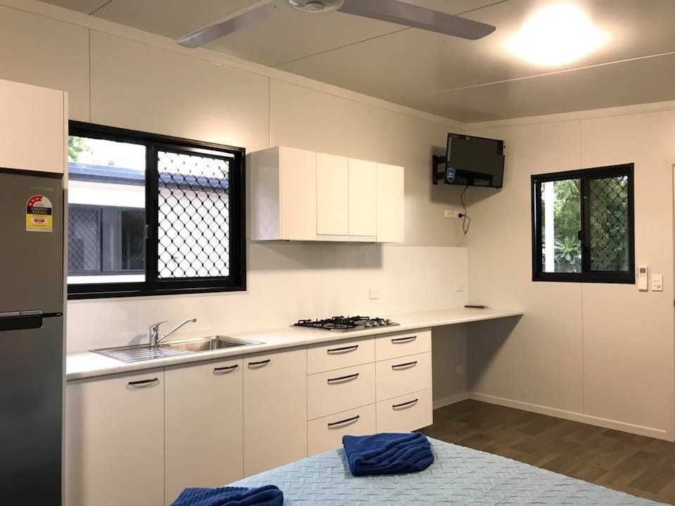 Bright White Kitchenette With Cabinets, Sink, Stove, and a Small Mounted Tv — Karumba Point Holiday Tourist Park in Karumba, QLD