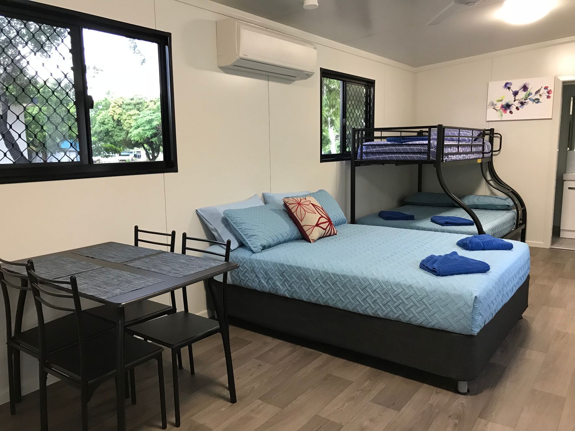 Bedroom With a Double Bed, Bunk Beds, Table, Chairs, Air Conditioner, and Two Windows — Karumba Point Holiday Tourist Park in Karumba, QLD
