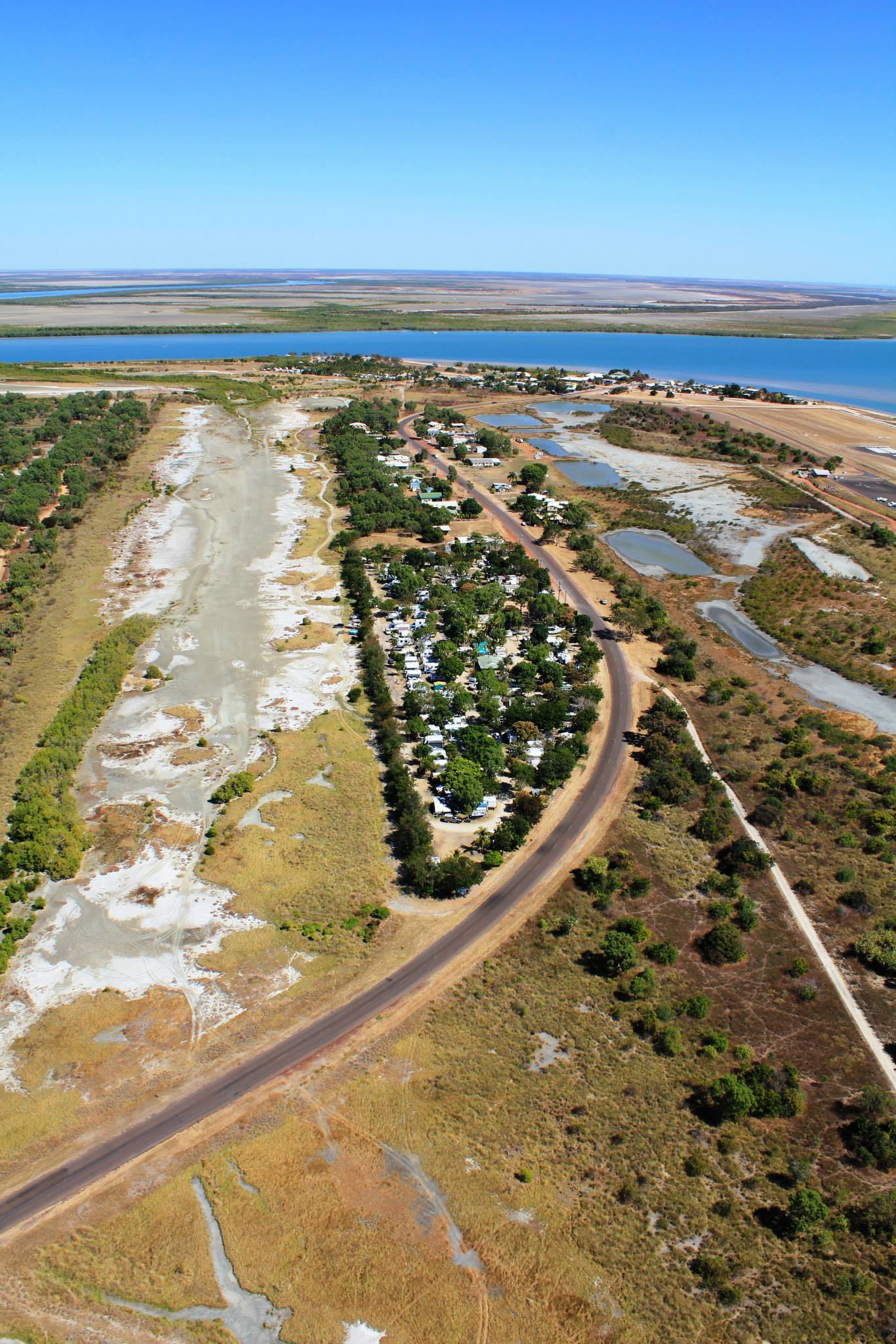 Aerial View: Road Winding Through a Green Area With a Settlement Beside a Large Body of Water — Karumba Point Holiday Tourist Park in Karumba, QLD
