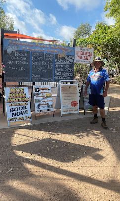 Man in Hat Stands Near Signs Advertising Tours and Fishing in Sunny Outdoor Area — Karumba Point Holiday Tourist Park in Karumba, QLD