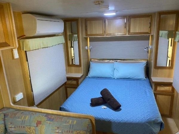 Bedroom in a Caravan With a Blue Bed, Matching Linens, and Wooden Cabinets — Karumba Point Holiday Tourist Park in Karumba, QLD