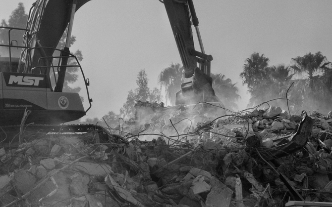 Excavator demolishing debris with dust rising at a rubble-strewn construction site