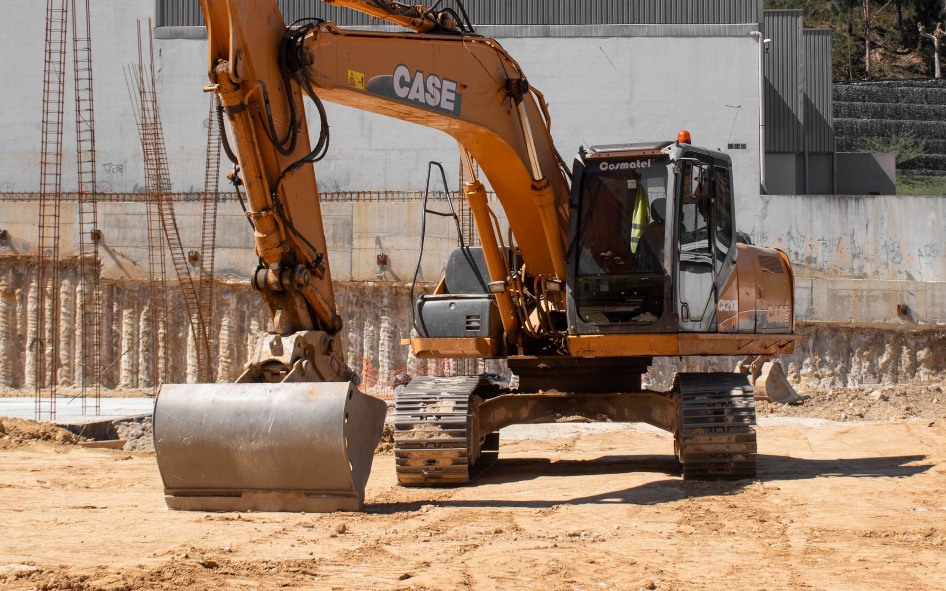 Orange excavator on a construction site with dirt piles and concrete walls