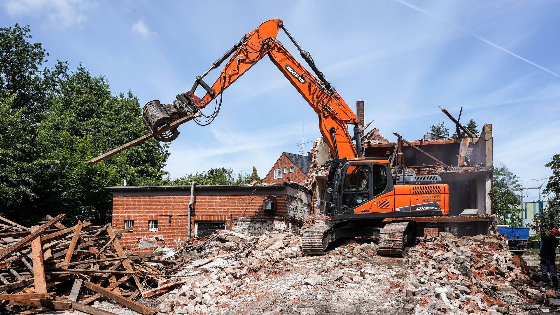 Orange excavator demolishing a brick building amid rubble on a construction site