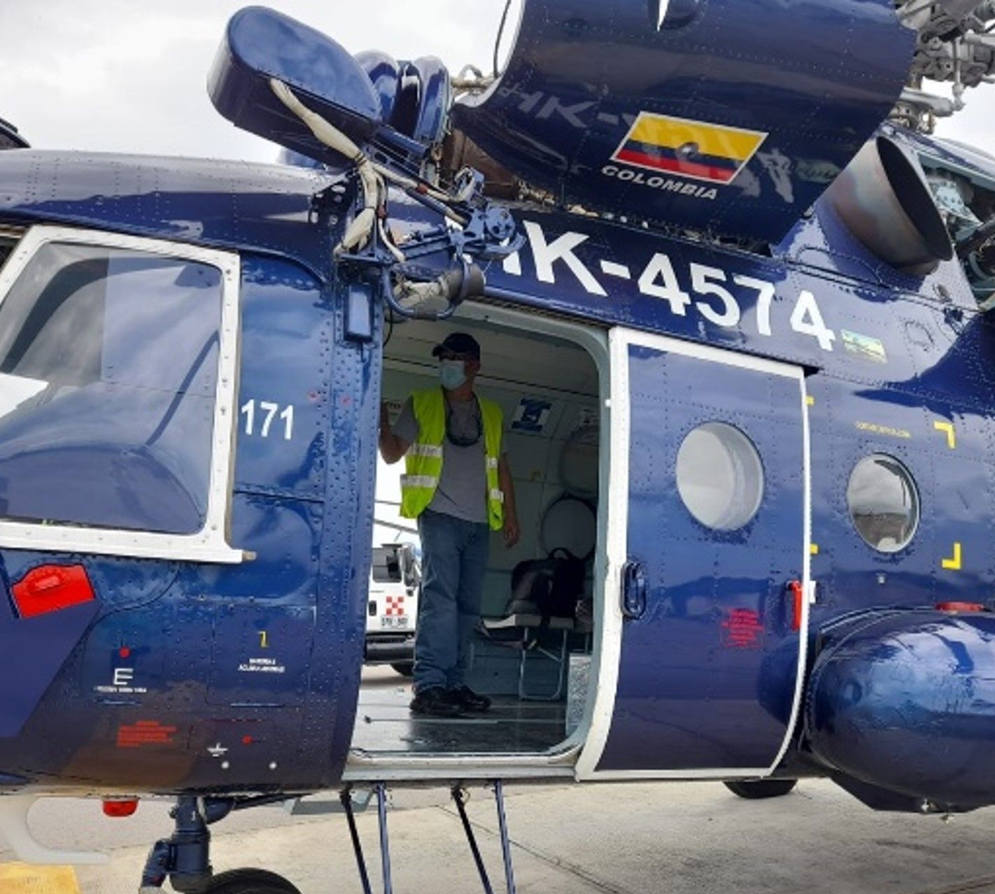 Helicóptero azul con puerta abierta, persona con chaleco de seguridad dentro.