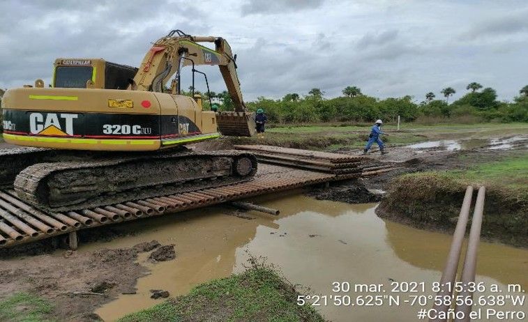 Una excavadora está sentada encima de un puente de madera sobre un río fangoso.